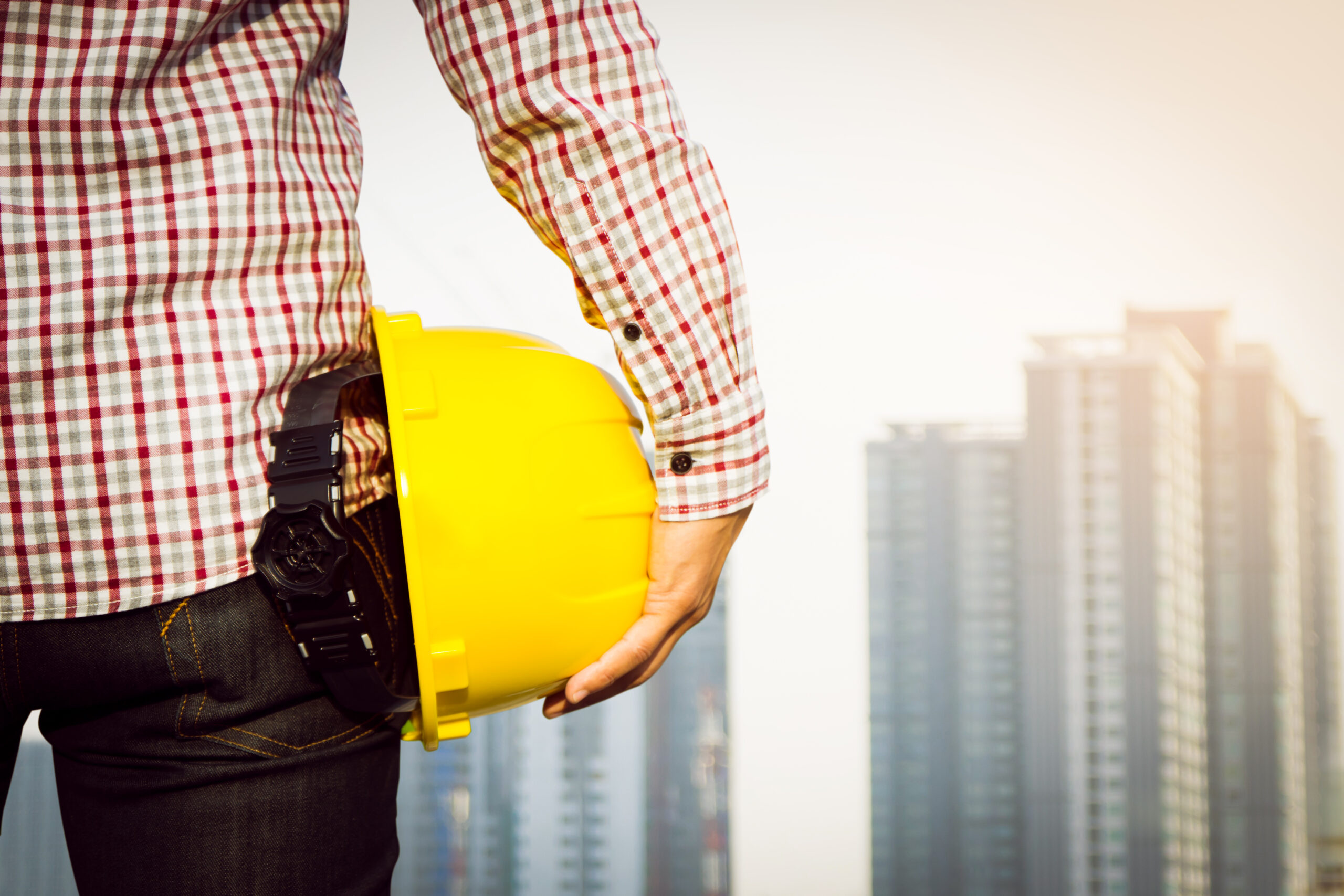 hand s engineer worker holding yellow safety helmet with building site background scaled